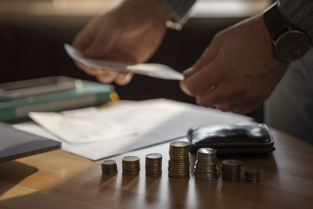 Homem mexendo em papeis, ao lado de uma pilha de moedas