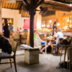 Imagem tem um blur de efeito, mas dá para perceber pessoas sentadas em várias mesas de um bar ou restaurante