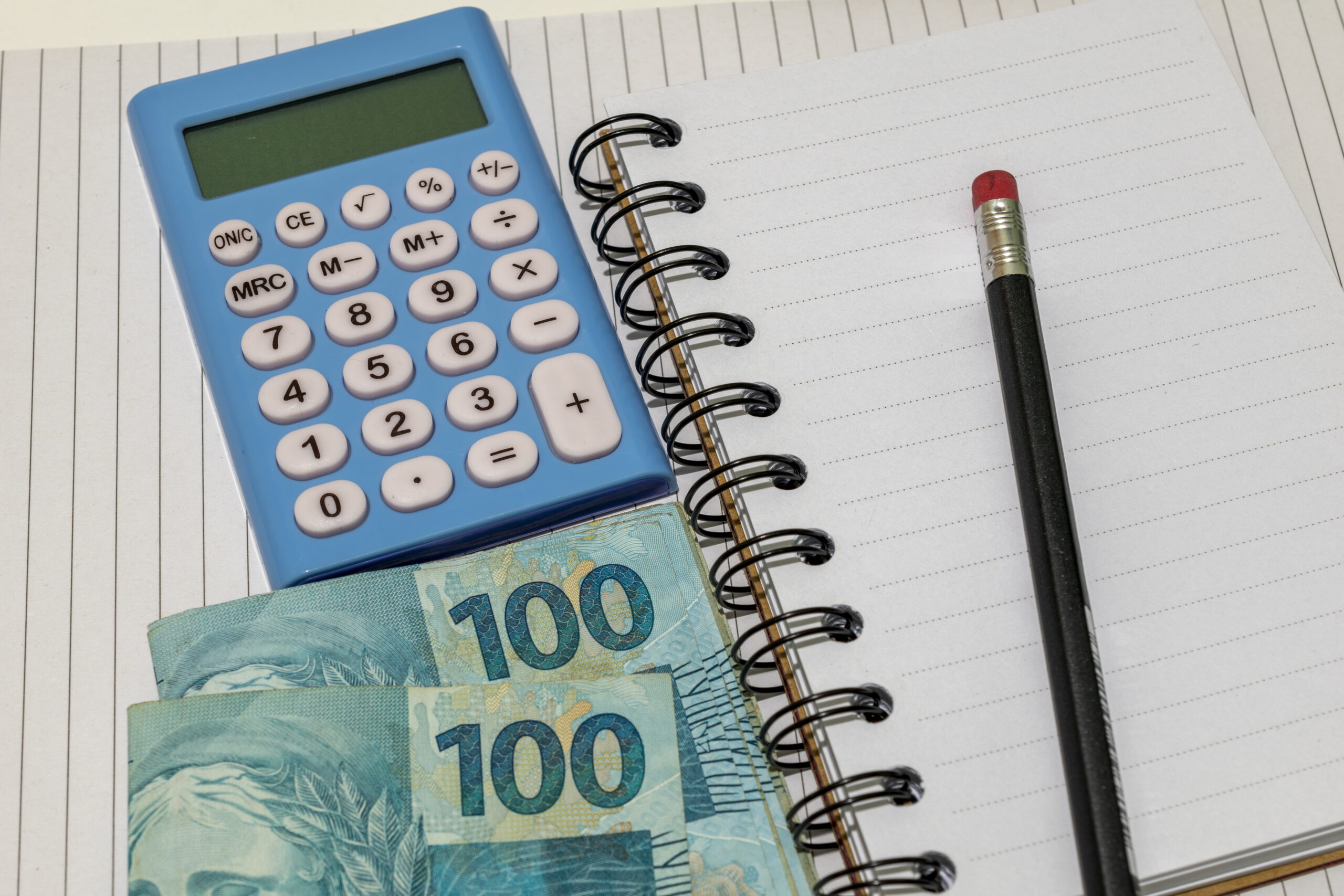 Uma calculadora ao lado de um lápis e duas notas de 100 reais